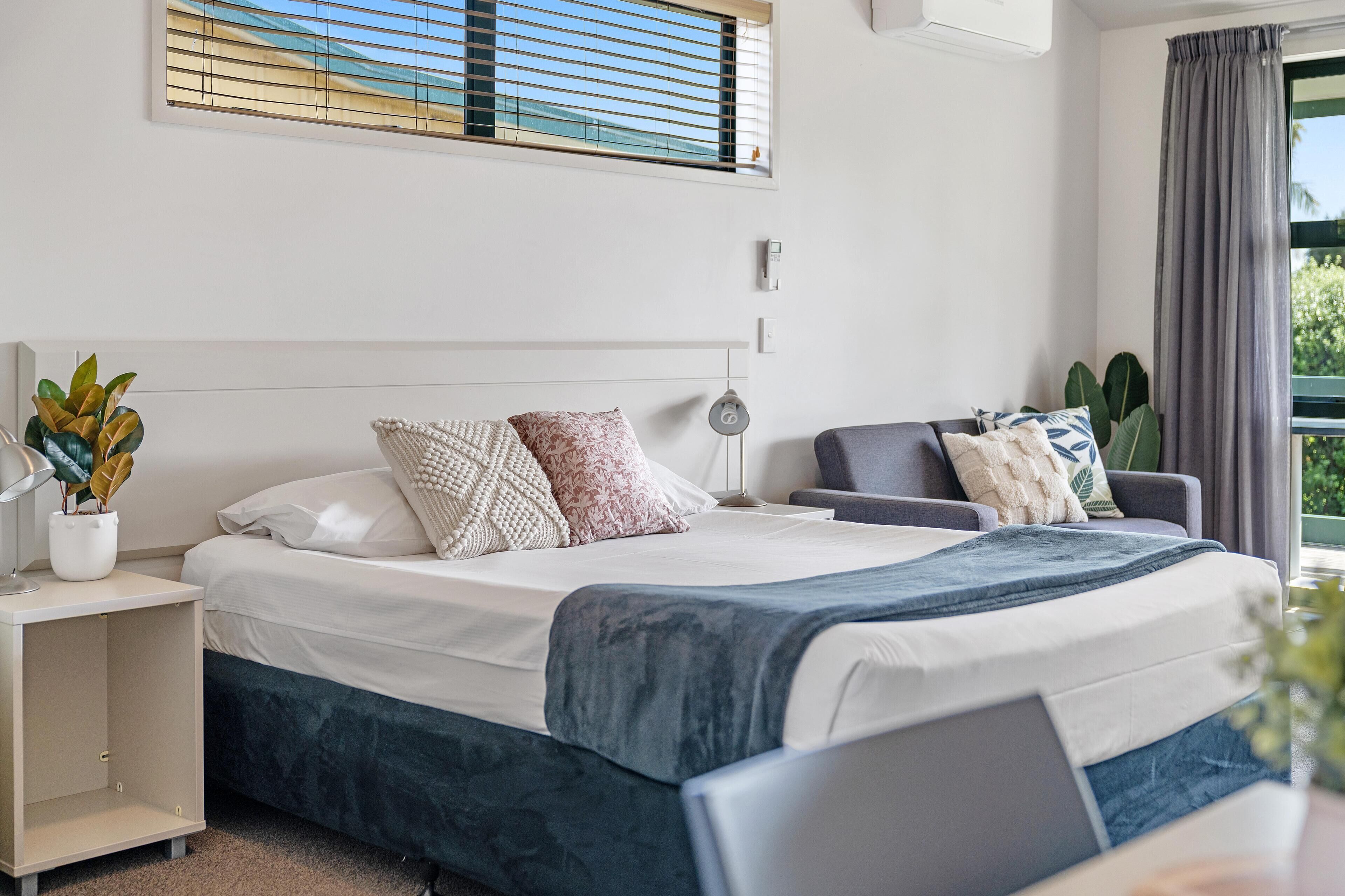 Quarto moderno com cama, mesa de cabeceira, abajur e vista para o exterior.
