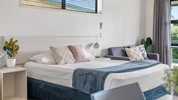 Quarto moderno com cama, mesa de cabeceira, abajur e vista para o exterior.