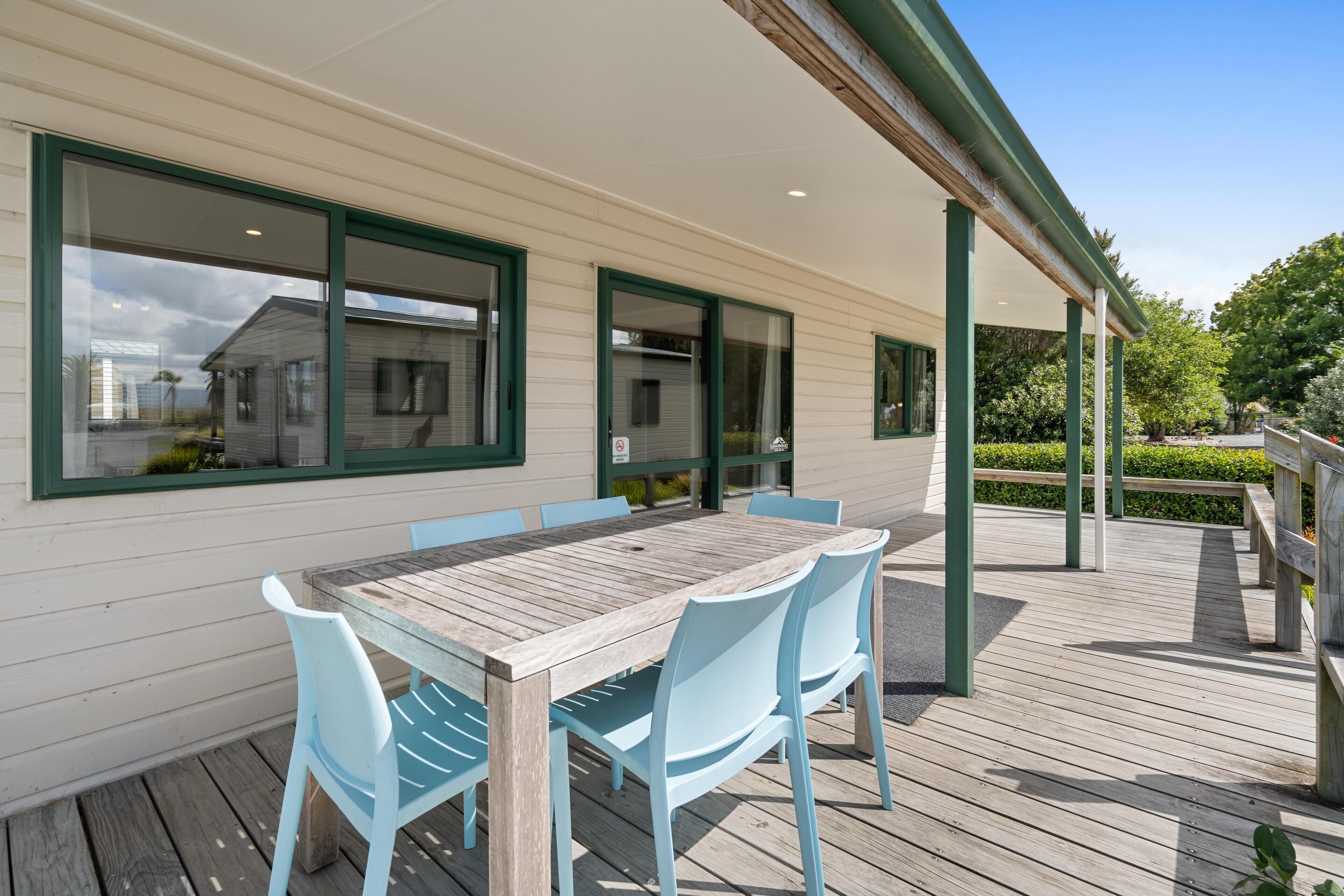 A wooden deck with a table and chairs, a covered patio area, and a view of a house through large windows.