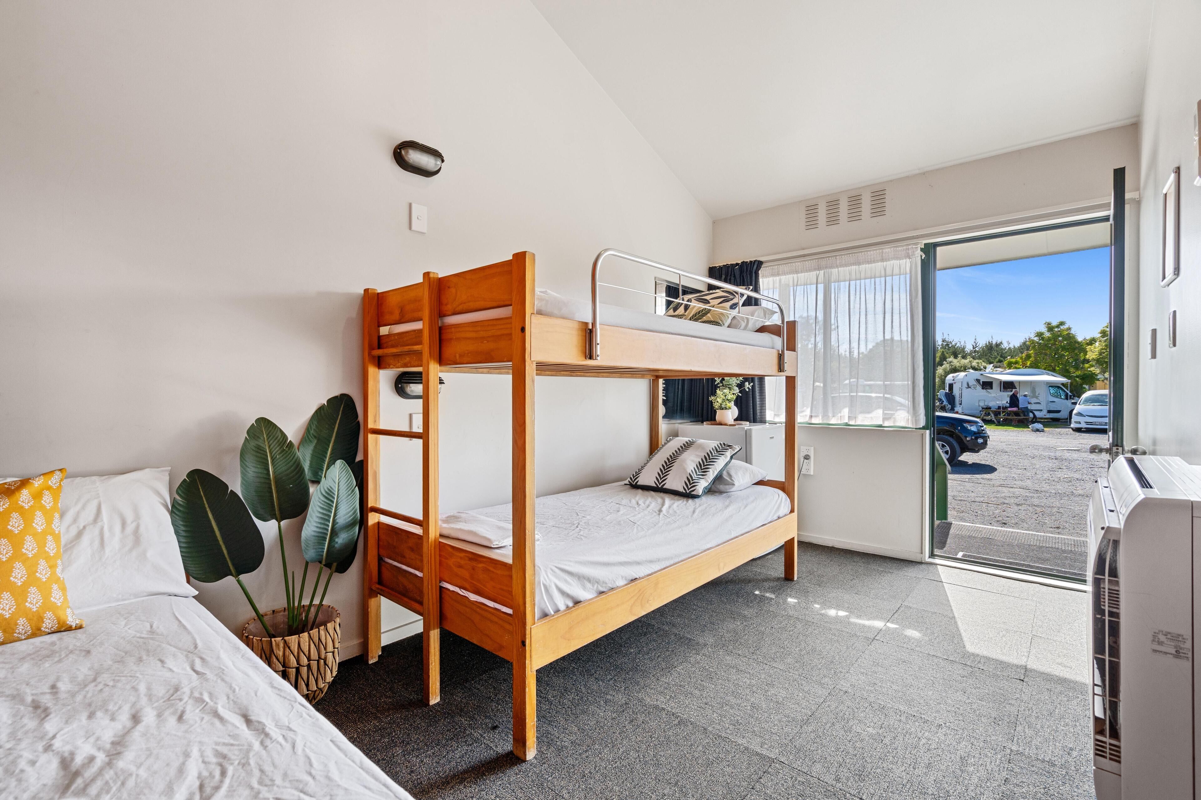 A bunk bed room with a window, a potted plant, and a door leading outside.