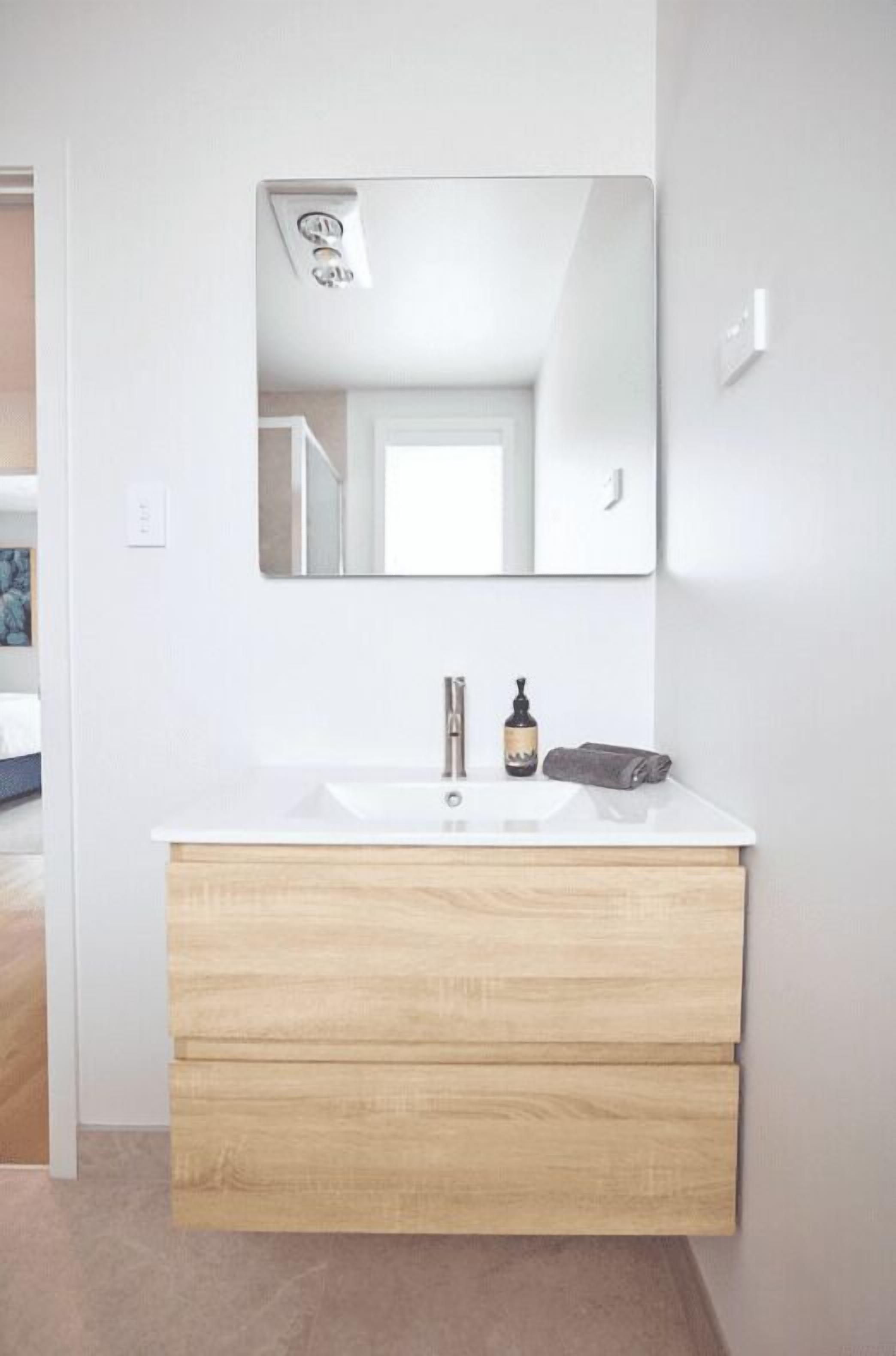 Un baño moderno con lavamanos blanco, tocador de madera y un espejo grande.