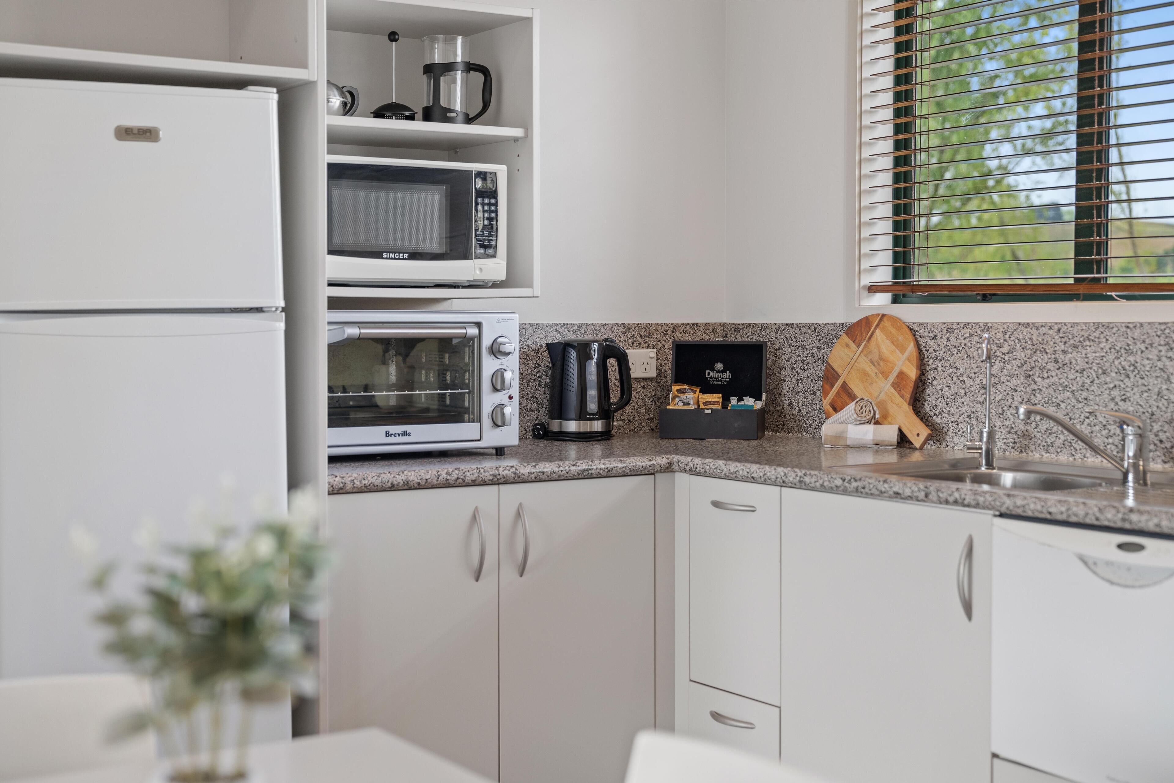 Cocina moderna con armarios blancos, microondas integrado, horno Breville y cafetera.