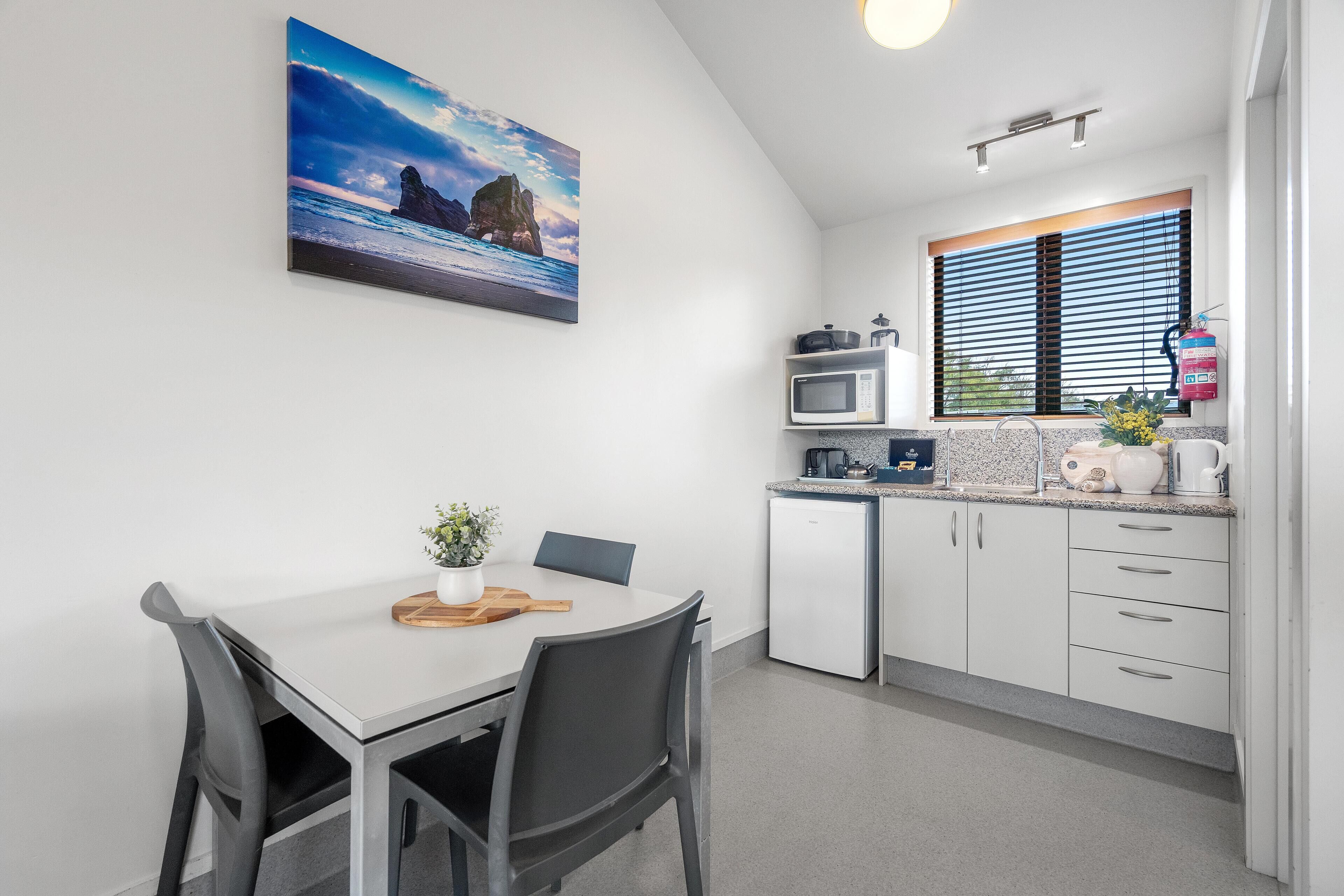 A modern kitchen with white cabinets, a microwave, and a window with blinds.