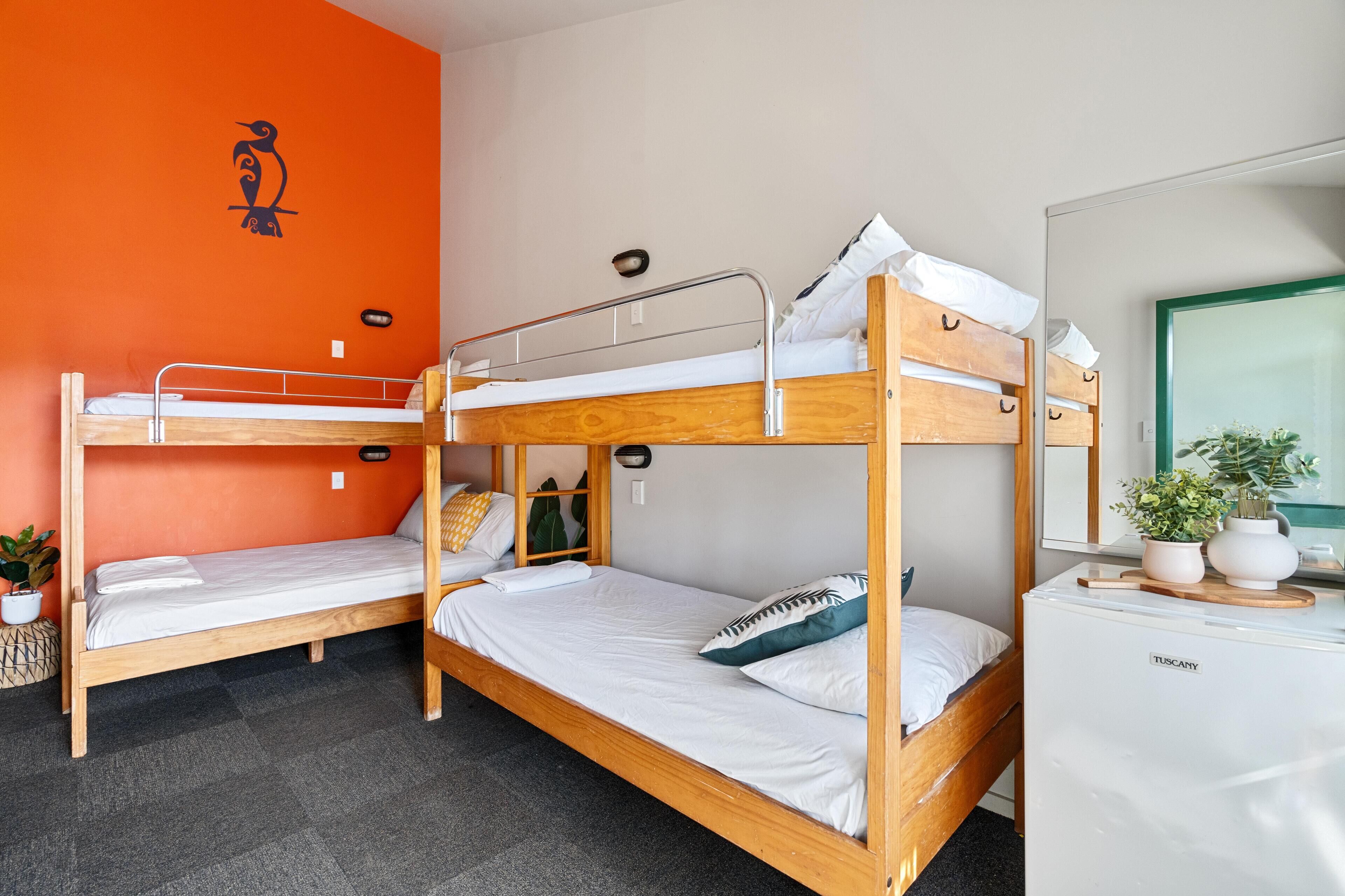 A room with two bunk beds, a wooden desk with a mirror, and a potted plant.