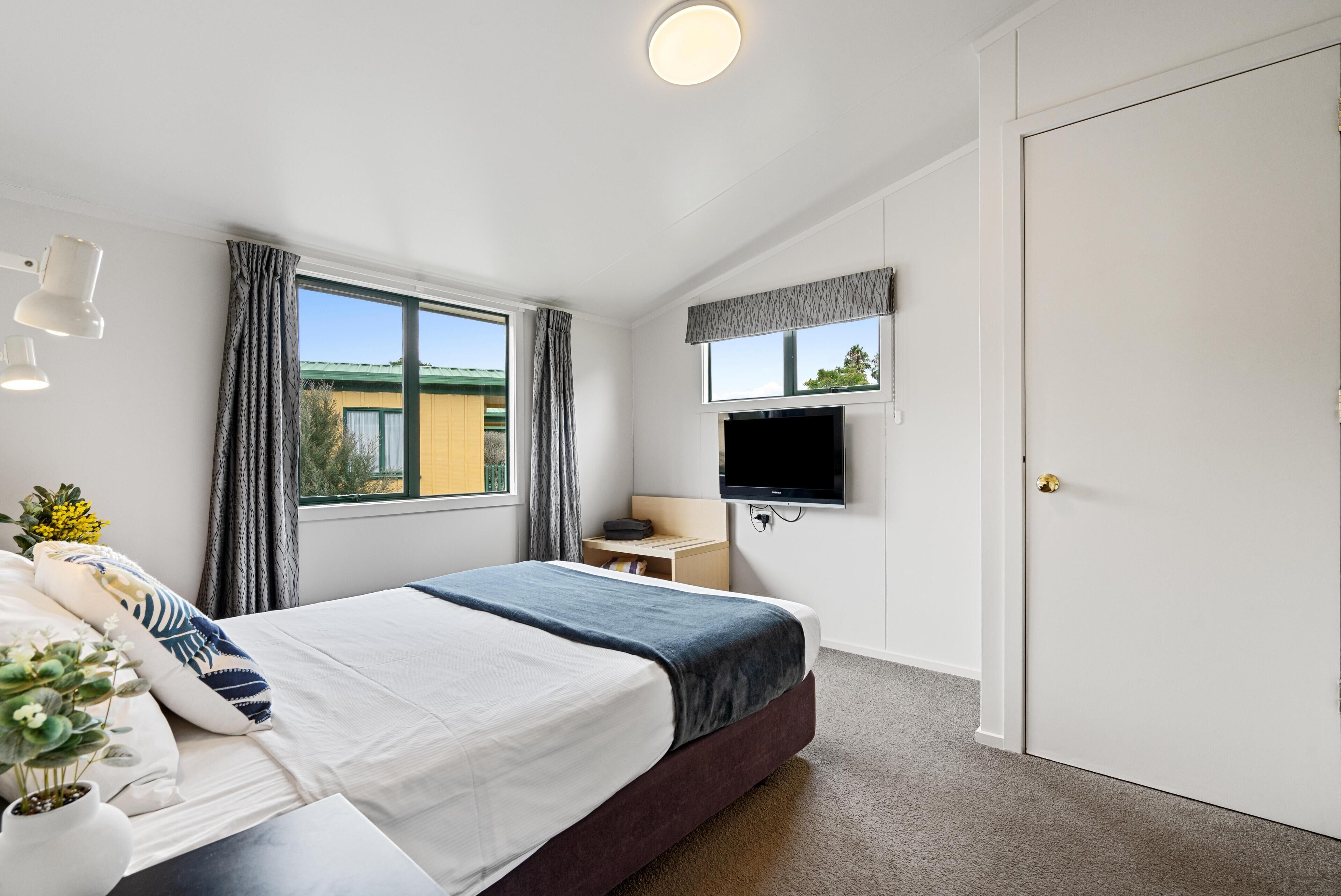 A hotel room with a bed, a desk, a TV, and a door.