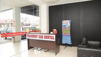 A reception desk labeled "TRACKWAY CAR RENTAL" with a signboard advertising a promotion.