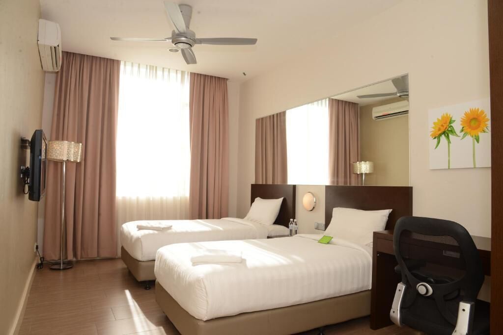 A hotel room with two beds, a ceiling fan, a mirror, a desk, a chair, and a window with curtains.