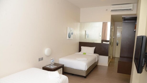 Quarto de hotel com duas camas, mesa de cabeceira com abajur, televisão de tela plana e ar-condicionado.