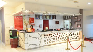 Bancada de receção de hotel em mármore, cortina de veludo vermelho e quadros nas paredes.