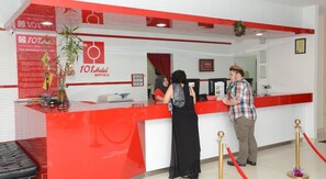 A reception desk with a red and white color scheme, a plant, and a framed certificate on the wall.