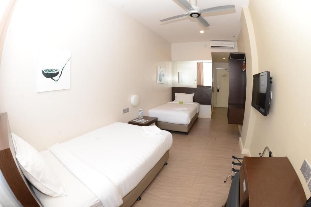 Habitación de hotel con una cama individual, un escritorio, una silla, un televisor y un ventilador de techo.
