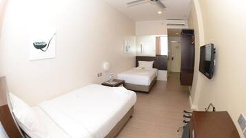 Habitación de hotel con una cama individual, un escritorio, una silla, un televisor y un ventilador de techo.