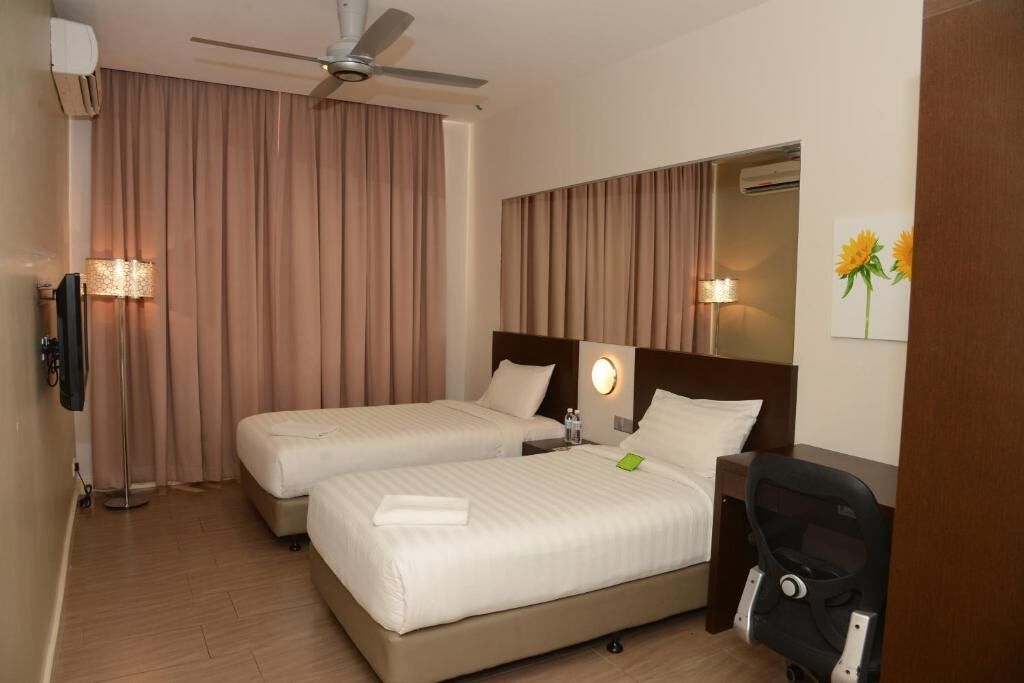 A hotel room with two beds, a ceiling fan, a TV, and a stroller.