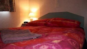 A bed with a red and pink patterned bedspread, a grey blanket, and a green headboard.