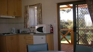 A compact kitchen with wooden cabinets, a microwave, a toaster, and a sink. There's a dining table with chairs and a sliding glass door leading to an outdoor area.