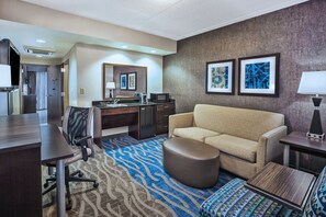 Una habitación de hotel con sofá, reposapiés, escritorio, silla y alfombra estampada.