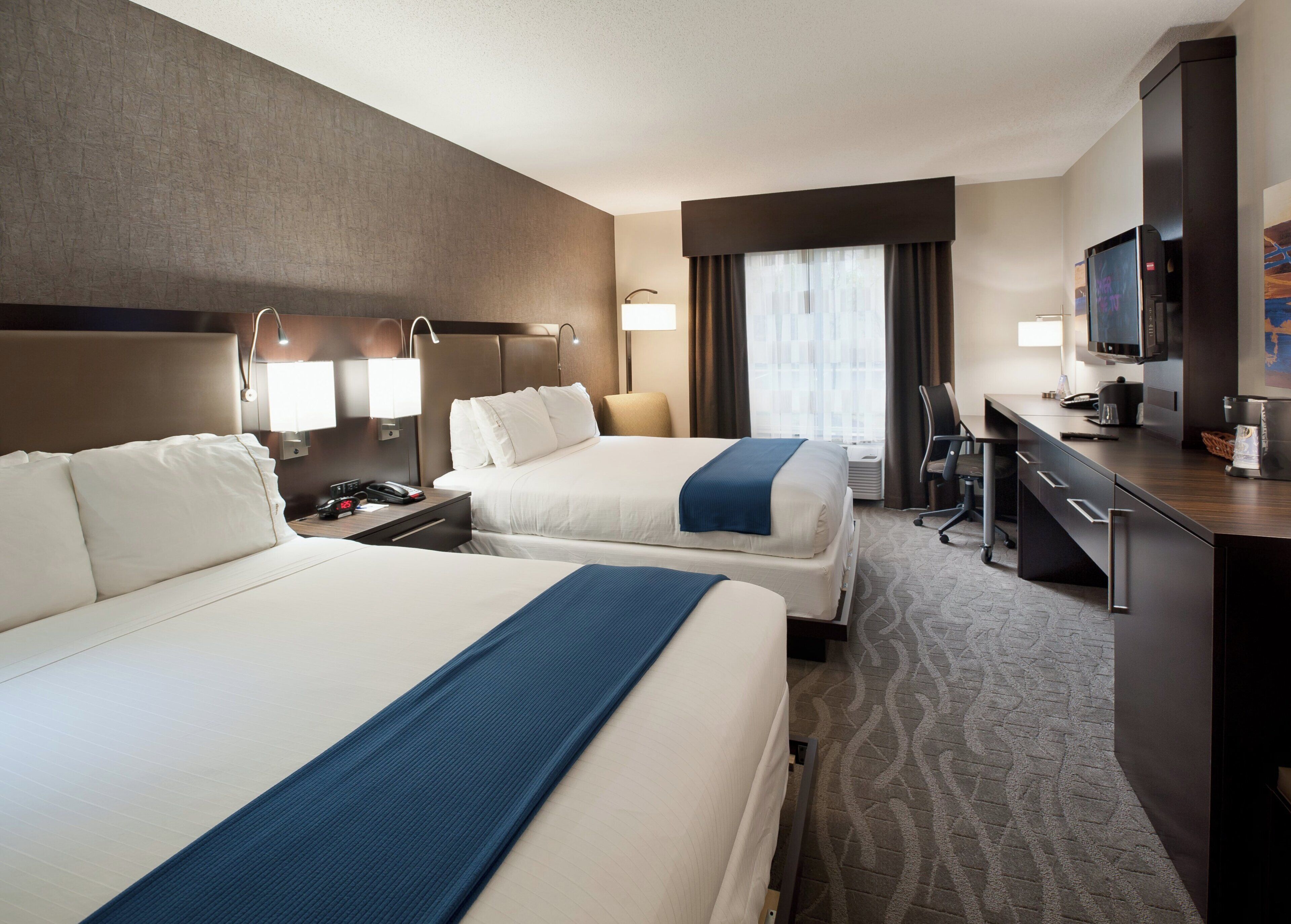 Une chambre d’hôtel avec deux lits, un bureau, une télévision et une fenêtre avec des rideaux.