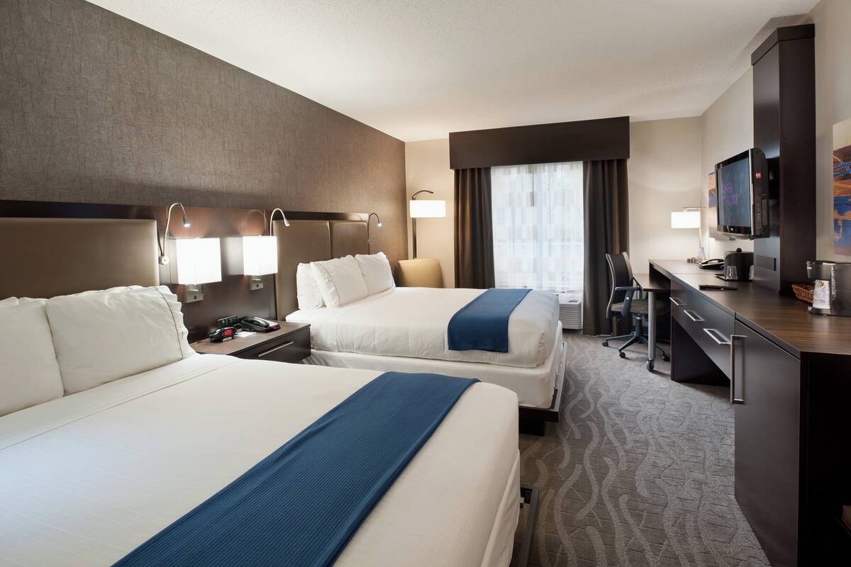 Habitación de hotel con dos camas, un escritorio, un televisor y una ventana con cortinas.