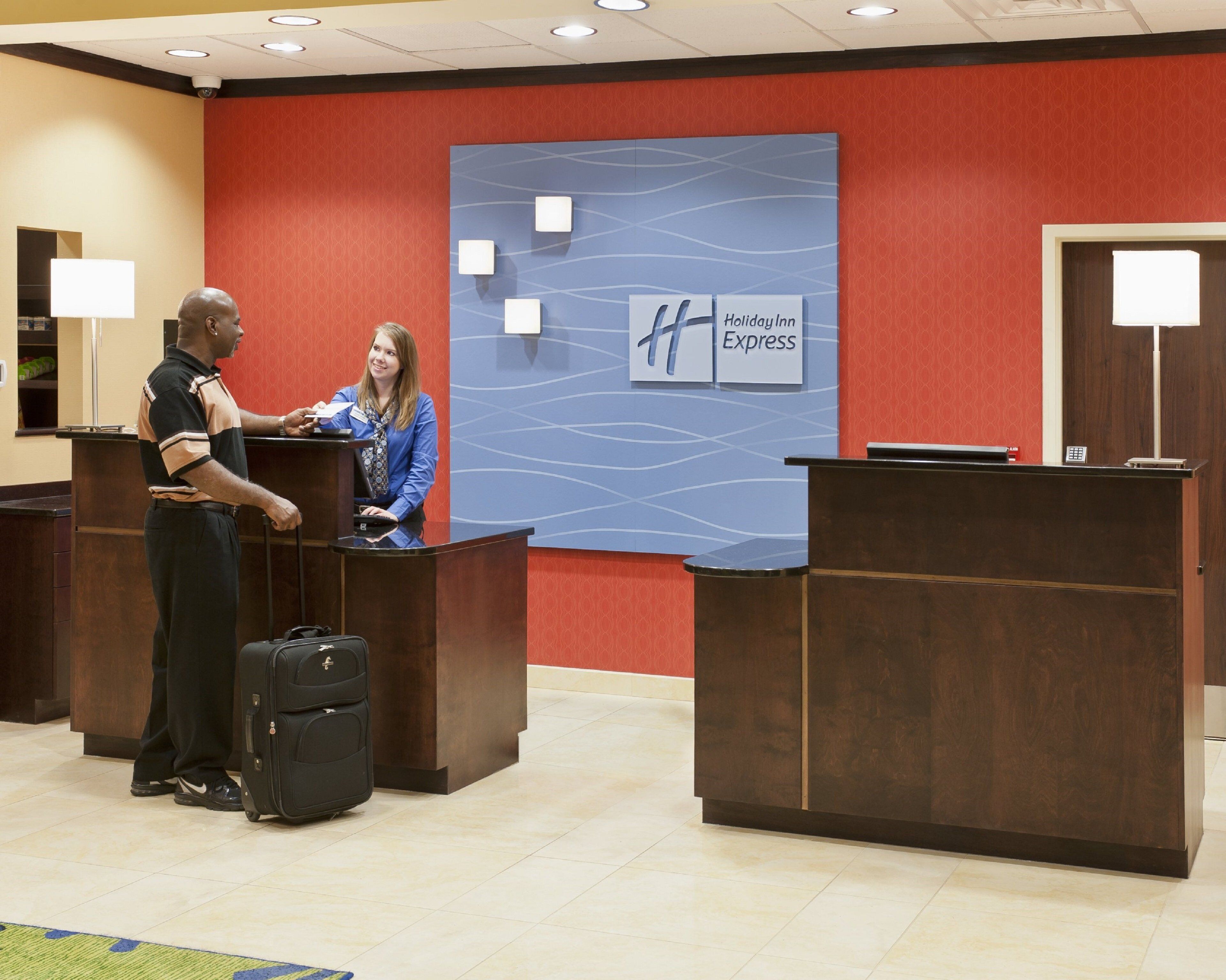 Un área de recepción con un letrero de Holiday Inn Express, un mostrador y un hombre entregando un documento a una mujer.