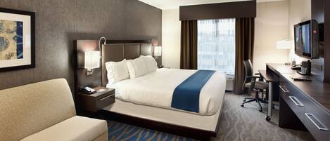 A hotel room with a bed, a desk, a chair, a sofa, a TV, and a framed picture on the wall.