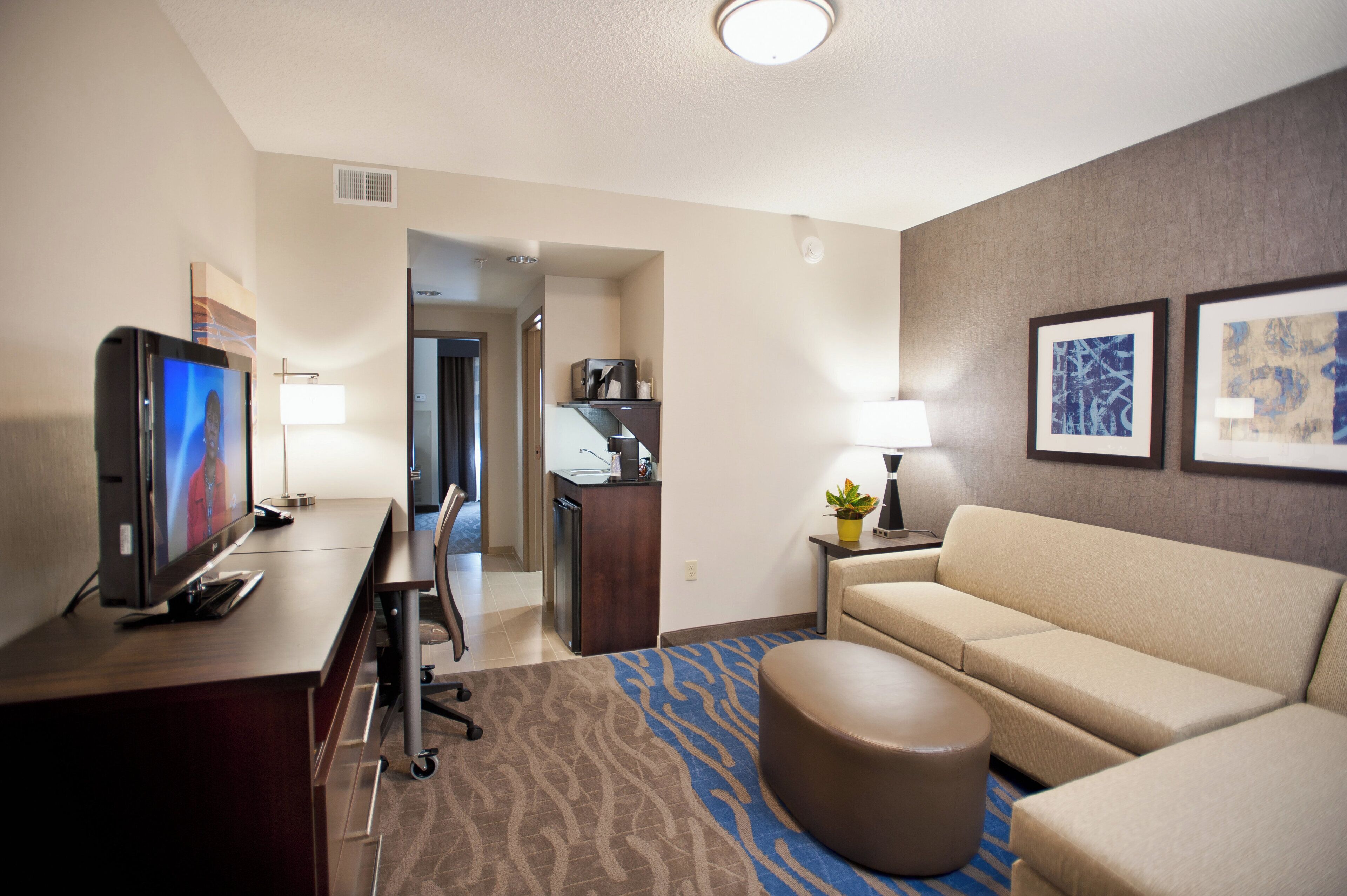 A hotel room with a flat-screen TV, a sofa, a coffee table, a desk, and a lamp.