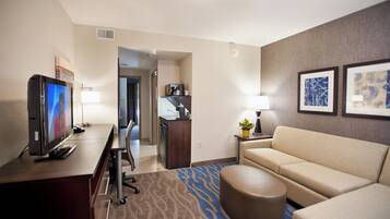 A hotel room with a flat-screen TV, a sofa, a coffee table, a desk, and a lamp.