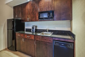 Eine kompakte Küche mit dunklen Holzausbau, einem Edelstahlkühlschrank, einer Mikrowelle, einem Geschirrspüler und einem Spülbecken.