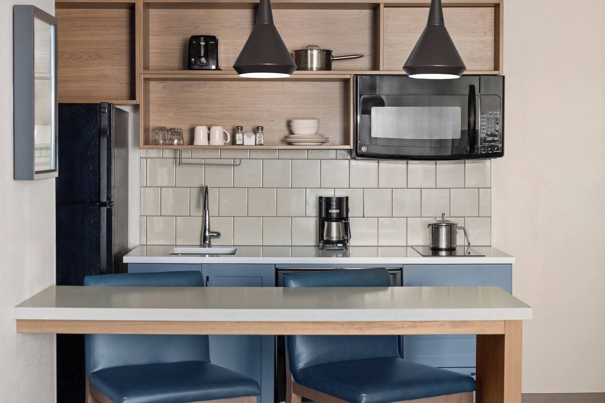 A modern kitchen with a built-in microwave, coffee maker, and a dining area with blue chairs.