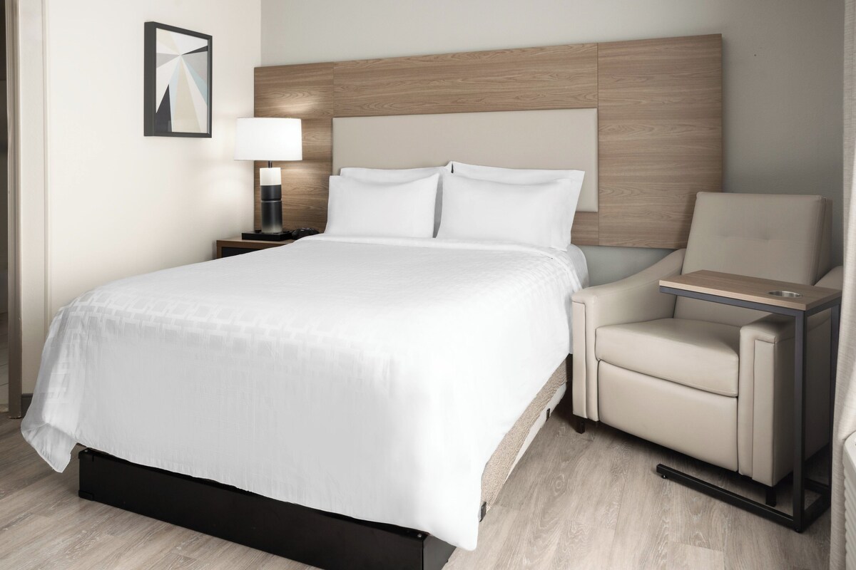 Une chambre d’hôtel avec un lit, une table de chevet avec une lampe, une chaise et une petite table.