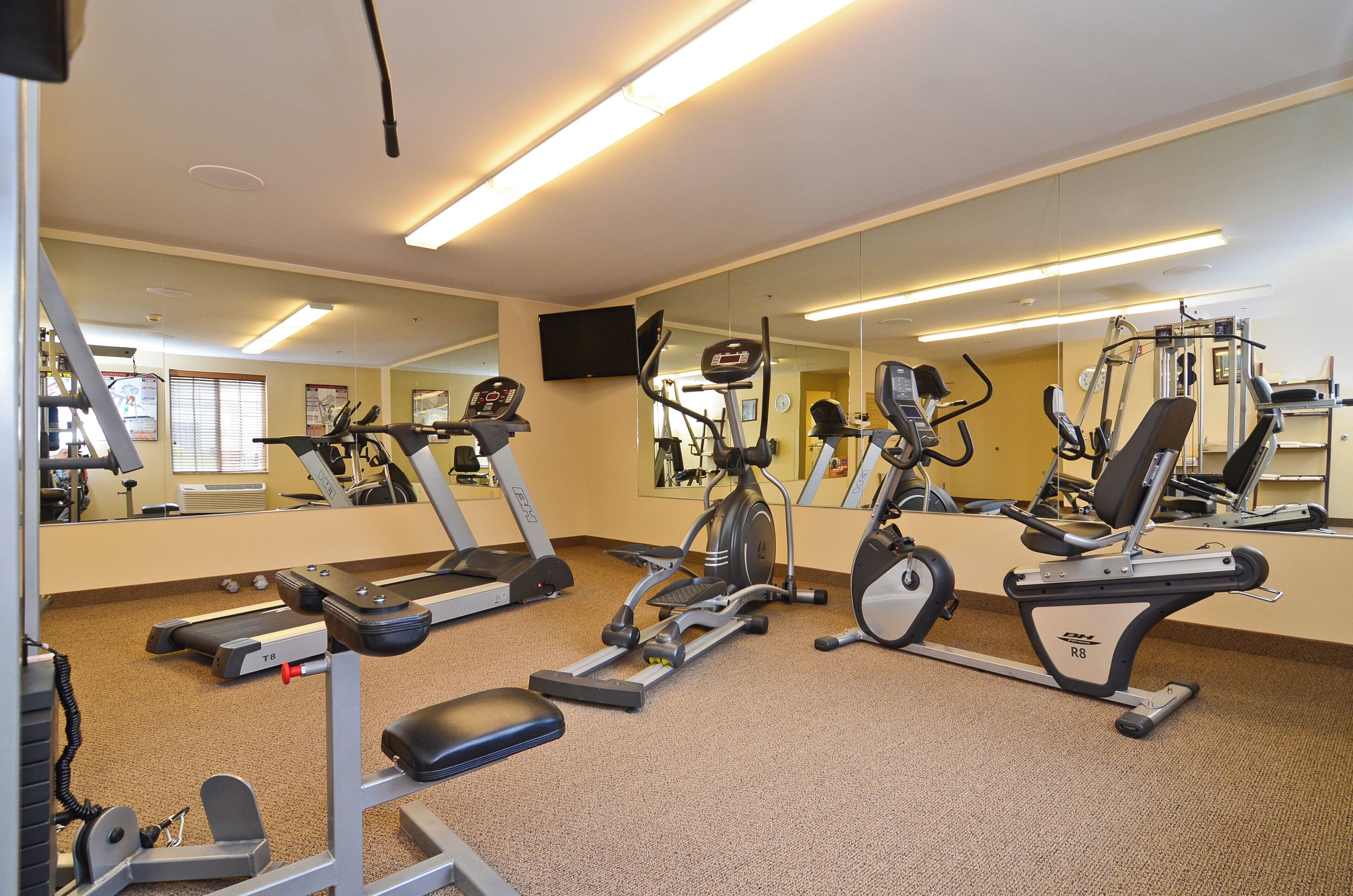 Een sportschool met diverse fitnessapparaten, waaronder loopbanden en hometrainers, en spiegels aan de muur.