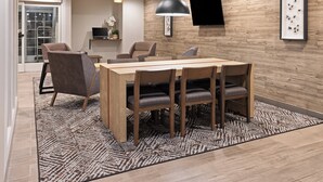 A modern dining area with a wooden table and chairs, a patterned rug, and a wall-mounted TV. - Candlewood Suites Chambersburg by IHG (Chambersburg)