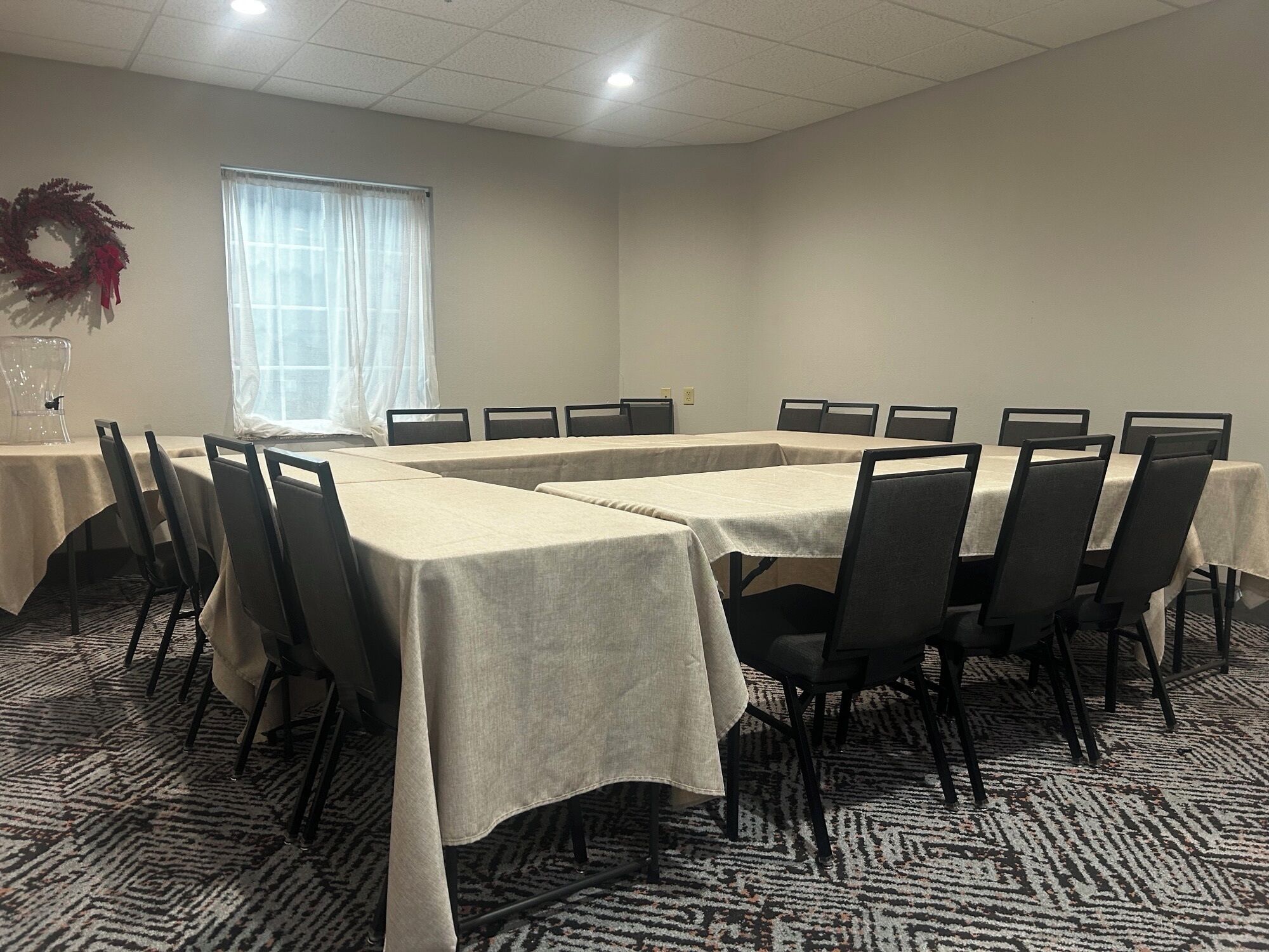 A conference room with a long table, chairs, a window with curtains, and a decorative wreath.