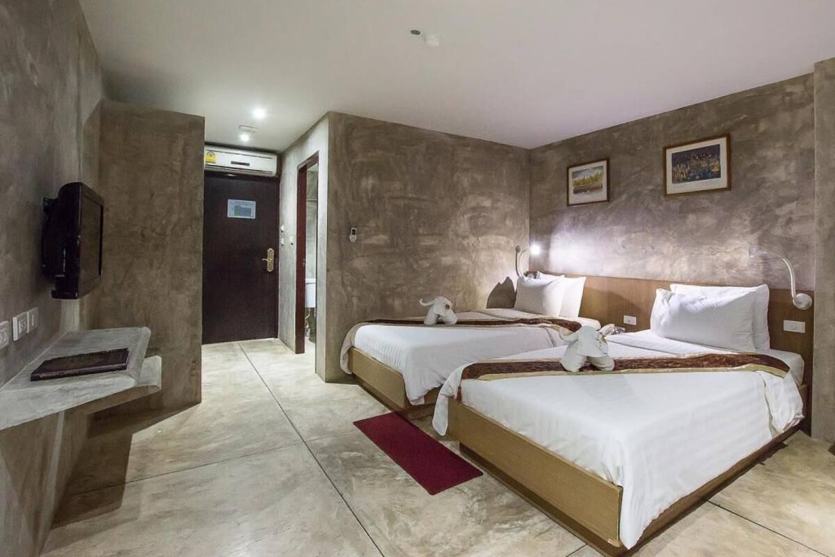 A hotel room with two beds, a flat-screen TV, a desk, and a red rug.