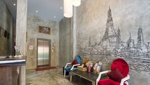 A reception area with a marble wall mural, a reception desk, two chairs, and an elevator. - Buddy Boutique Inn (Bangkok)