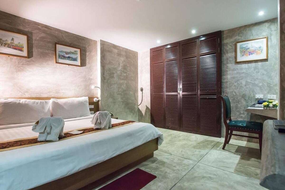 A hotel room with a bed, a desk with a chair, and a wardrobe.