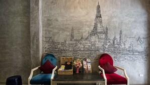 A room with two red chairs, a small table with a vase of flowers, and a wall mural of a cityscape. - Buddy Boutique Inn (Bangkok)
