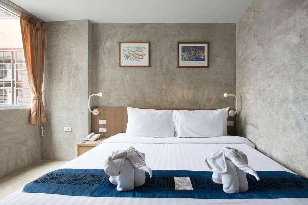 A hotel room with a large bed, two framed artworks on the wall, a bedside table with a lamp, and a window with curtains.