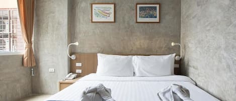 A hotel room with a large bed, two framed artworks on the wall, a bedside table with a lamp, and a window with curtains.