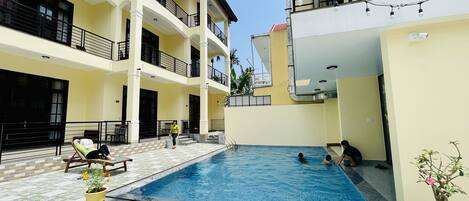 A swimming pool area with tiled flooring, a pool, and potted plants.