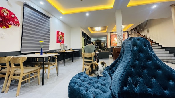A modern living room with a blue sofa, wooden chairs, a dining area, and a staircase. - Windbell Villa (Da Nang)