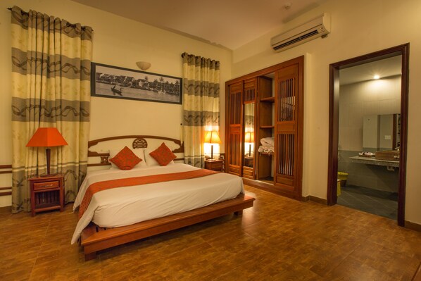 A well-lit hotel room with a large bed, wooden headboard, and a wooden wardrobe.