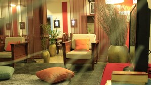 A cozy living room with a sofa, armchairs, and a coffee table. There are books and a vase with plants on the table. - Heart Language Angkor Hotel - Hostel (Siem Reap)