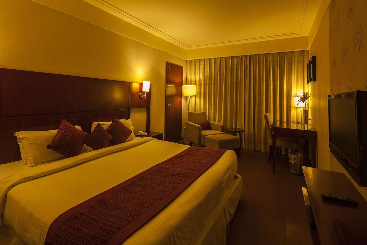 A hotel room with a large bed, a desk, a chair, a TV, and a lamp.