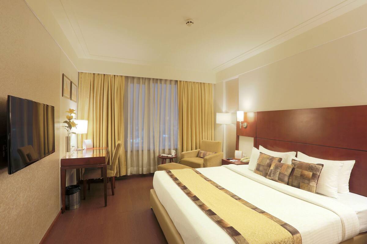 A hotel room with a large bed, a desk with a chair, a small table, and a lamp.
