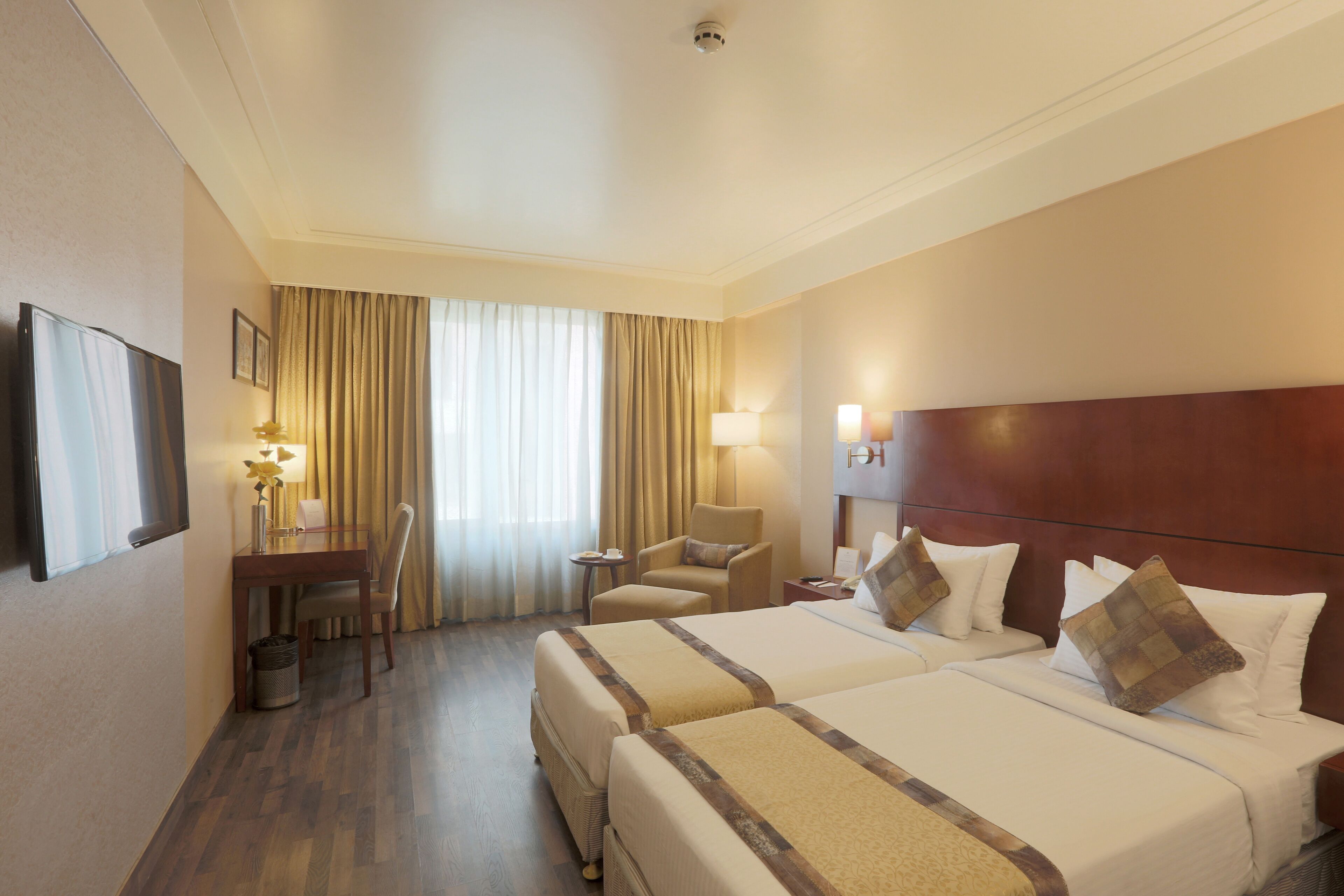 Quarto de hotel com duas camas, uma escrivaninha, uma cadeira e uma televisão.