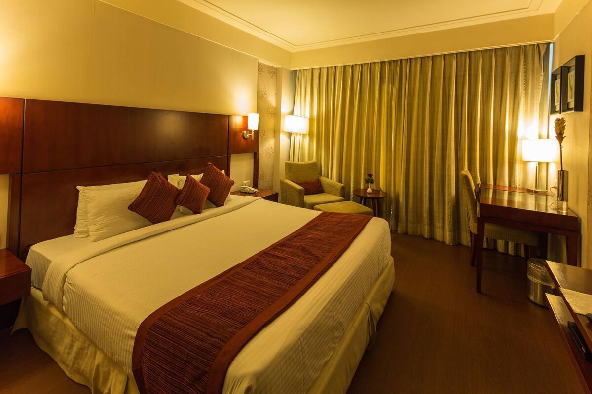 A hotel room with a large bed, a desk, a chair, a lamp, and a curtain.