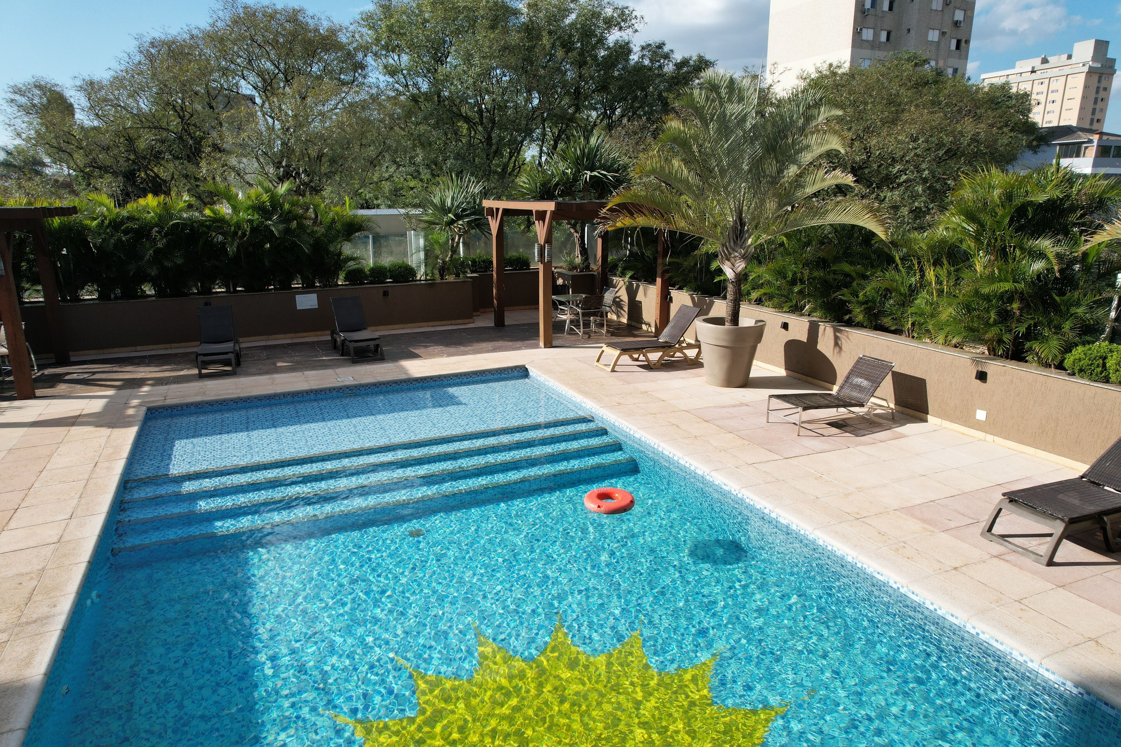 Une piscine avec des marches permettant d’y accéder, entourée de chaises longues et d’une pergola.