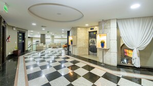 En hotellobby med ett rutmönstrat golv, en receptionsdisk, en trappa och en bardisk.
