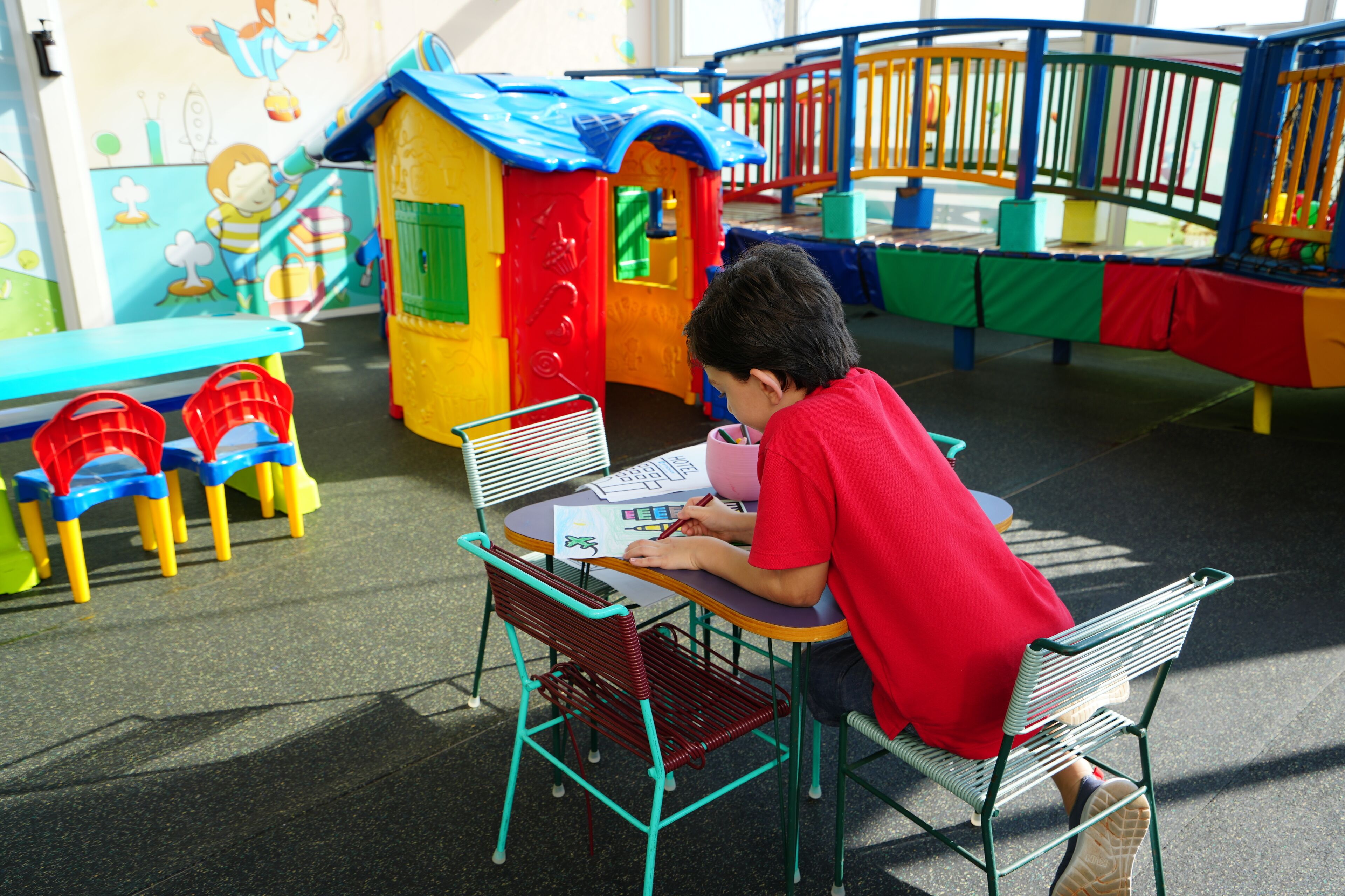 A child sitting at a table with a colorful play area in the background.