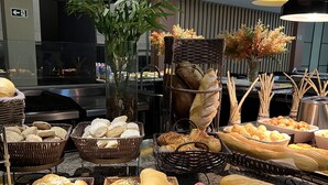 En buffé med olika sorters bröd och bakverk, en växt och en skylt som visar att det finns ”Pão Frances”, ett franskt bröd.